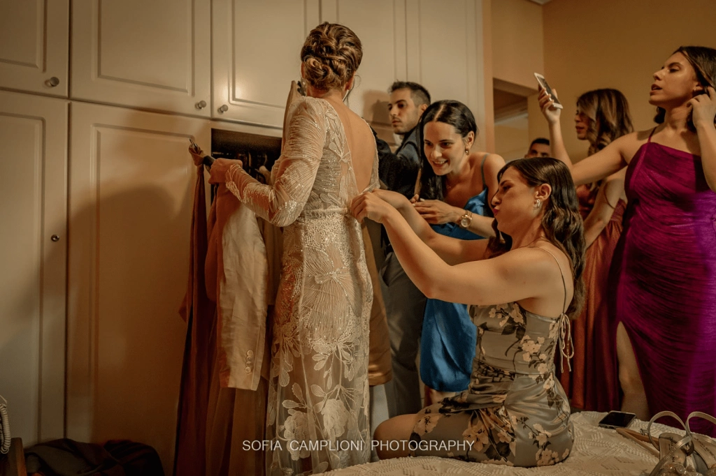 image of a koumbara helping her greek bride put on her wedding dress