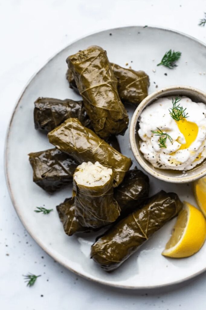 A picture of Greek Dolmades, which is stuffed grape leaves with rice, and yogurt.