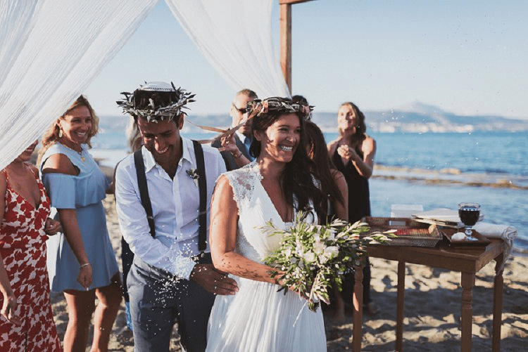 Bride and groom walk happily after the beachfront ceremony in Greece while guests throw rice to them. 