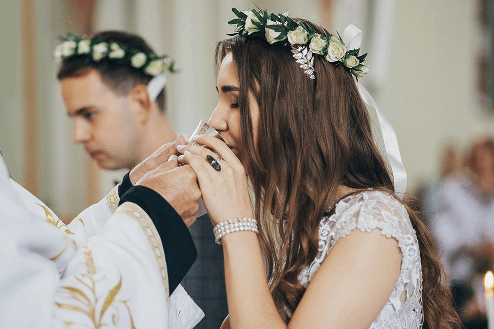 Bride and groom sharing wine from the common cup during their Greek Orthodox wedding ceremony, representing unity.