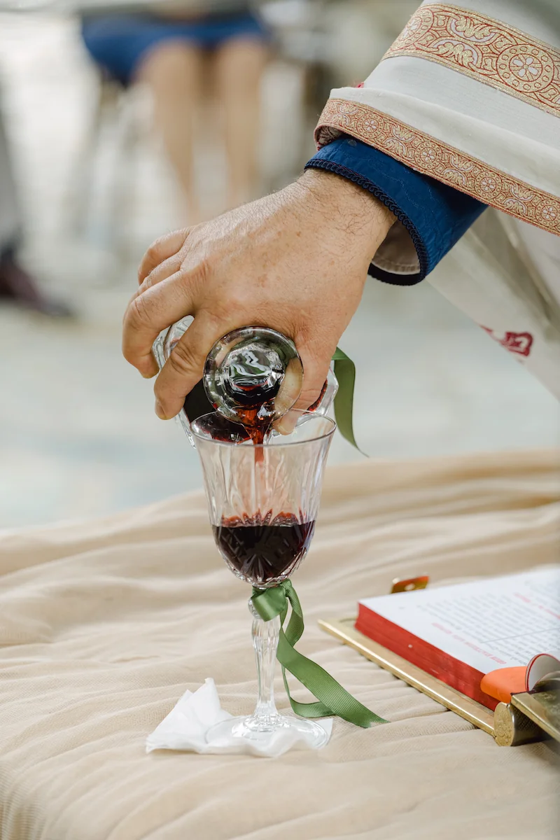 a greek orthodox priest pour red win into a crystal wine glass for the common cup ritual