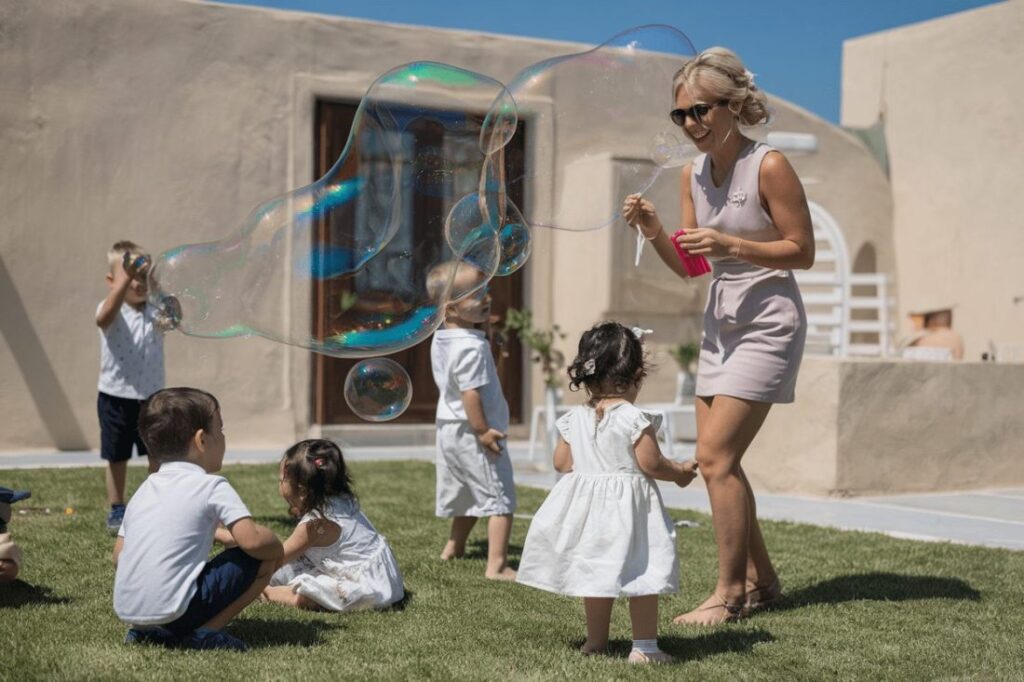 A joyful scene of children playing on a grassy area while a woman blows large bubbles, creating a fun and engaging atmosphere for a kid-friendly wedding.