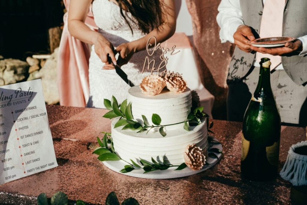 A bride and groom cutting a wedding cake adorned with flowers and greenery, next to a party schedule on a menu.