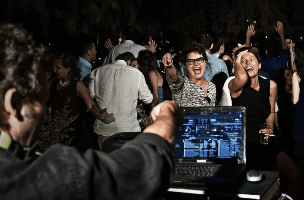 an image at a Greek wedding with the DJ pointing at two ladies dancing