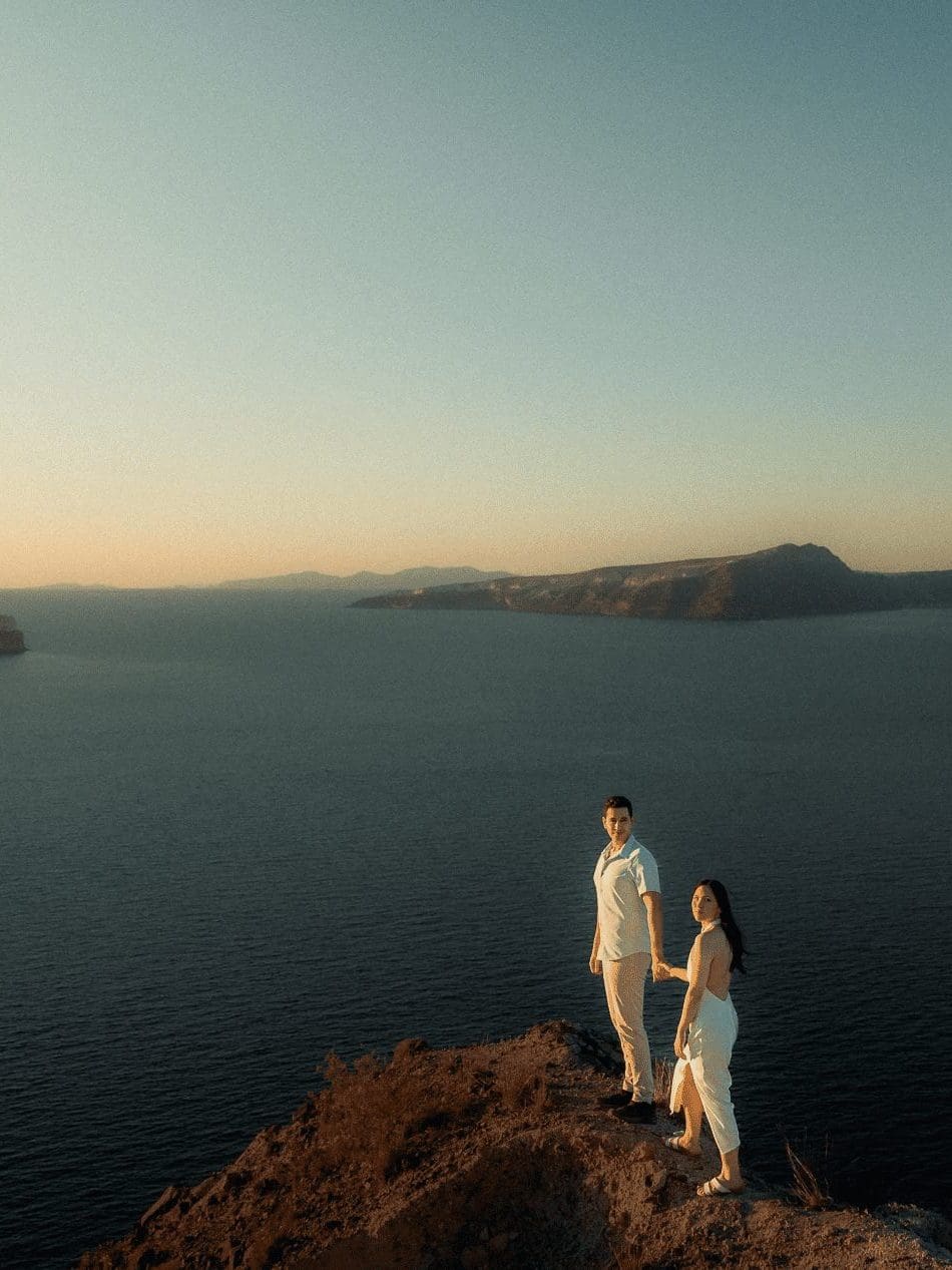 Couple which is organizing their destination wedding in Greece are standing at the edge of the hill, while the sea is unveiled in front of them.