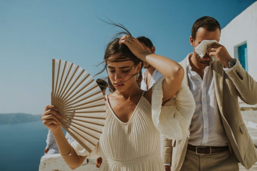 a bride and groom fanning themselves in the hot greek weather