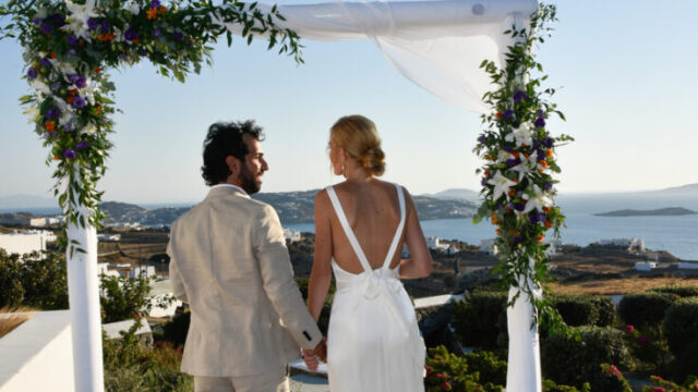 bride and groom stand in front of a wedding arch at aletro cottage houses in mykonos greece