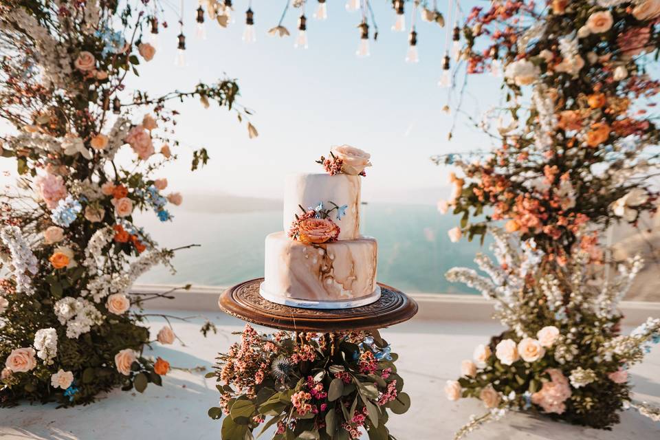 a beautifully decorated cake with flowers overlooking the santorini caldera