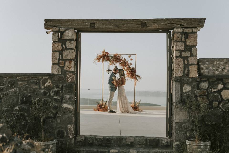 bride and groom embracing framed by a stone doorway in santorini