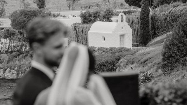 bride and groom with a white greek orthodox chapel in the distant background
