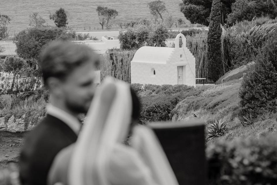 bride and groom with a white greek orthodox chapel in the distant background
