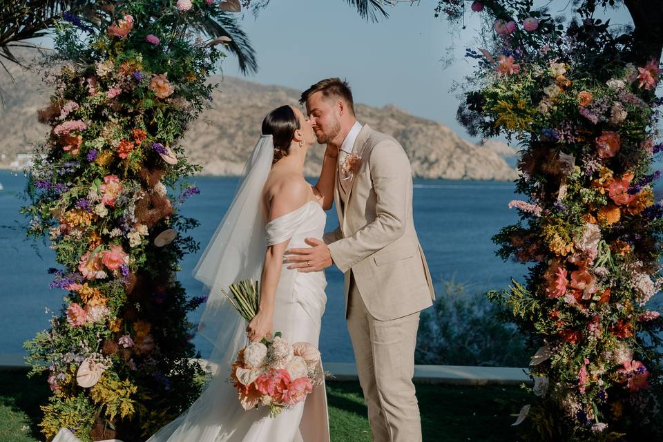 bride and groom kissing under a wedding arch in greece