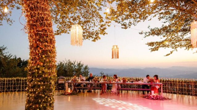 a colorfully lit greek wedding dance floor in the golden hour with the mountains in the background