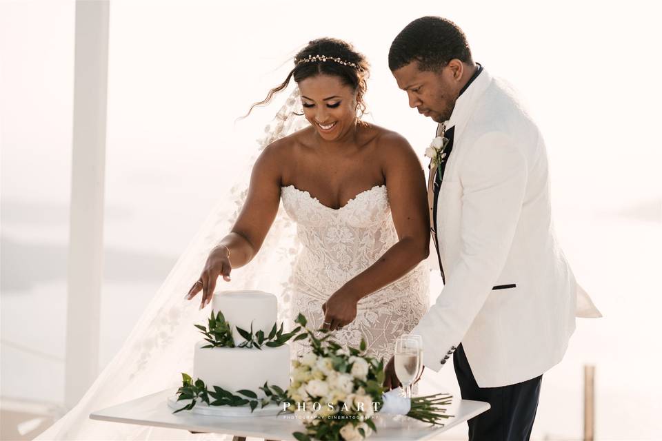 a couple cutting the cake at their wedding in santorini