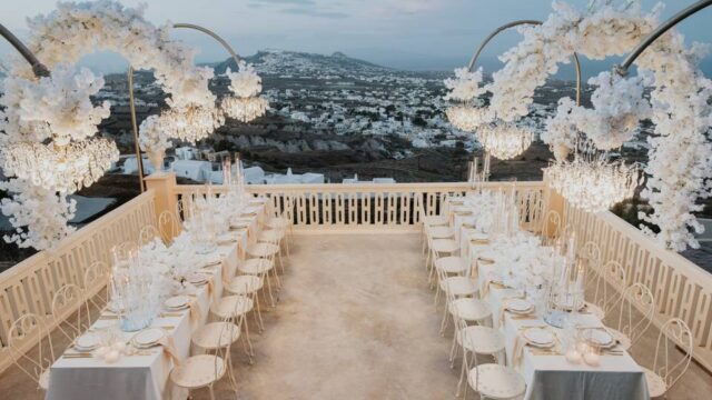 a dramatically beautiful view of tables set for a santorini wedding dinner