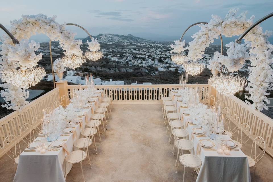 a dramatically beautiful view of tables set for a santorini wedding dinner
