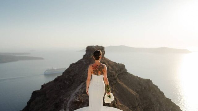 a bride with her back to the camera with an imposing backdrop of the greek mountains and sea