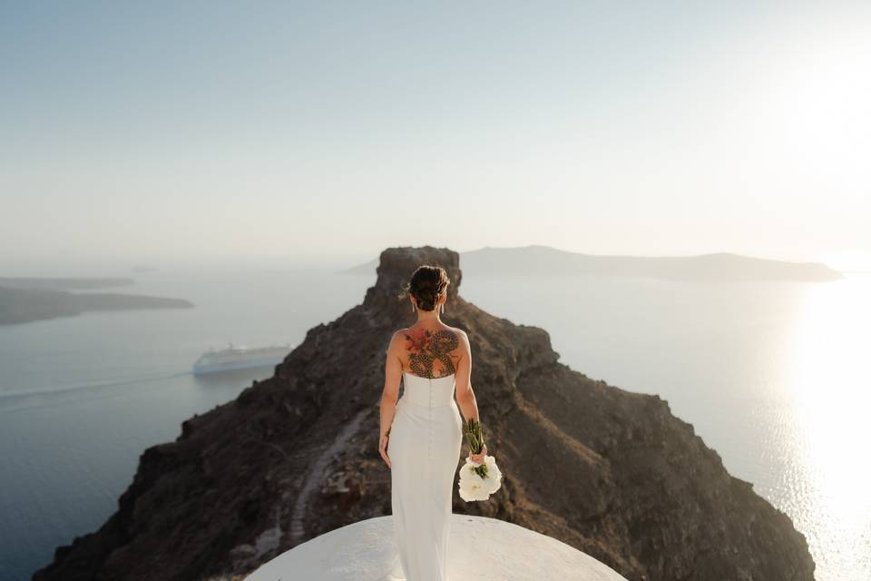 a bride with her back to the camera with an imposing backdrop of the greek mountains and sea