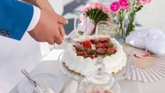 bride and groom both cutting the cake at a greek wedding