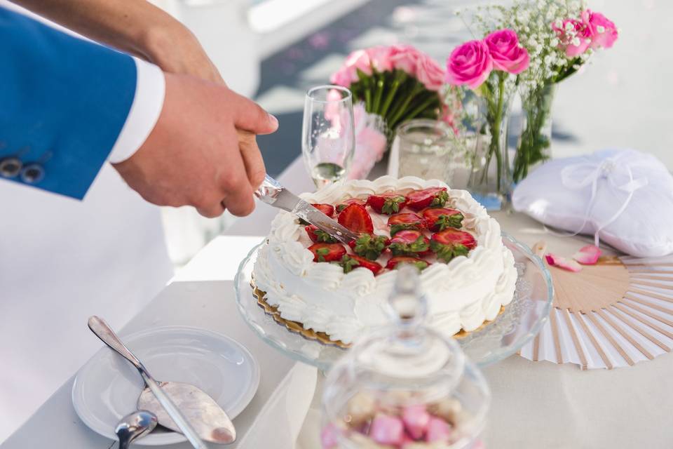 bride and groom both cutting the cake at a greek wedding