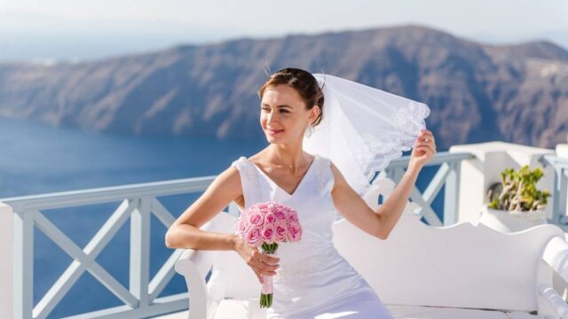 a brid holder her veil and flowers in front of the santorini caldera