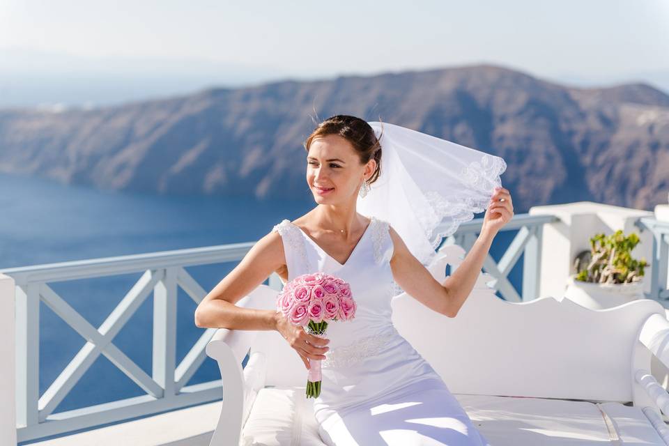 a brid holder her veil and flowers in front of the santorini caldera