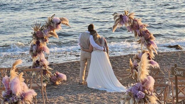 A couple looking at the sea on the beach at their greek wedding
