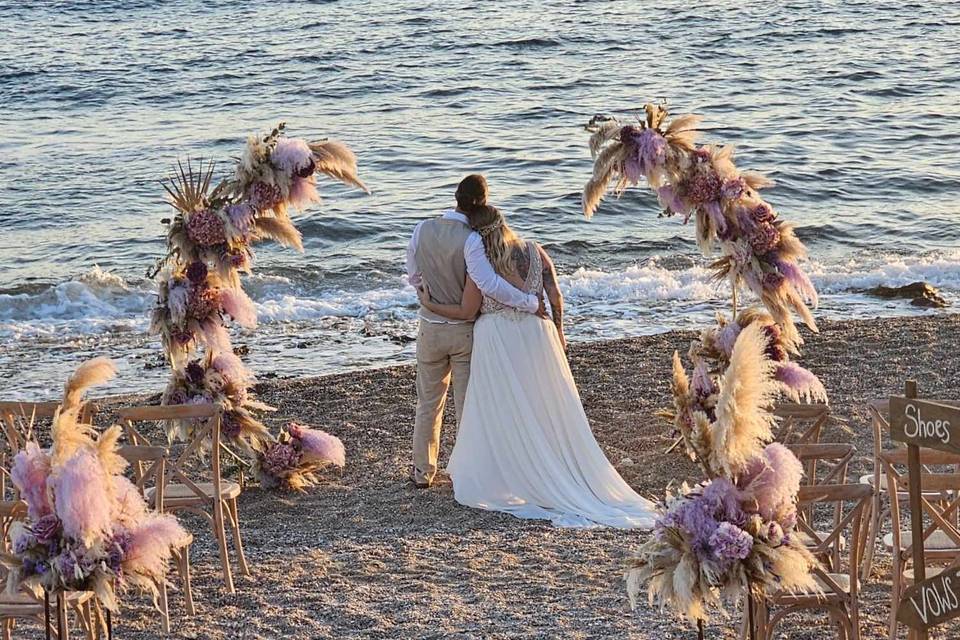 A couple looking at the sea on the beach at their greek wedding