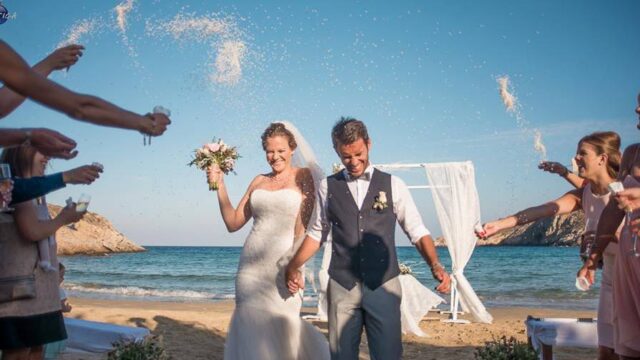 a bride and groom being showered with rice at their beach greek wedding