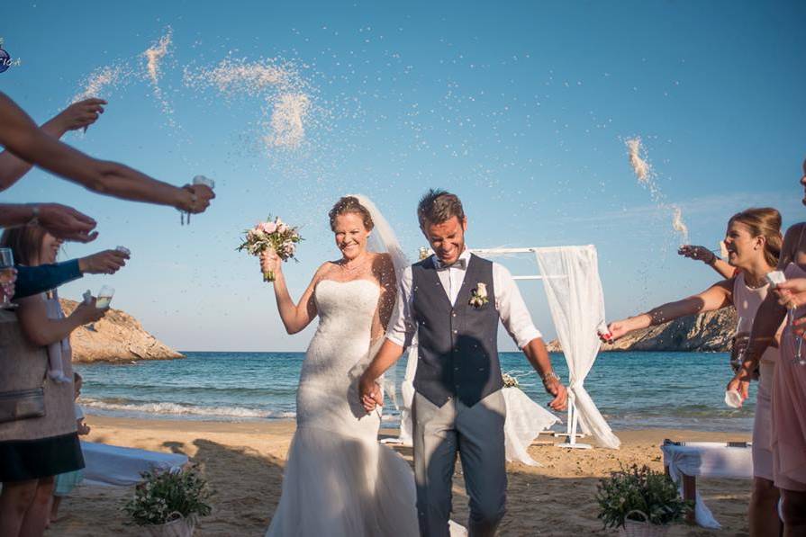 a bride and groom being showered with rice at their beach greek wedding