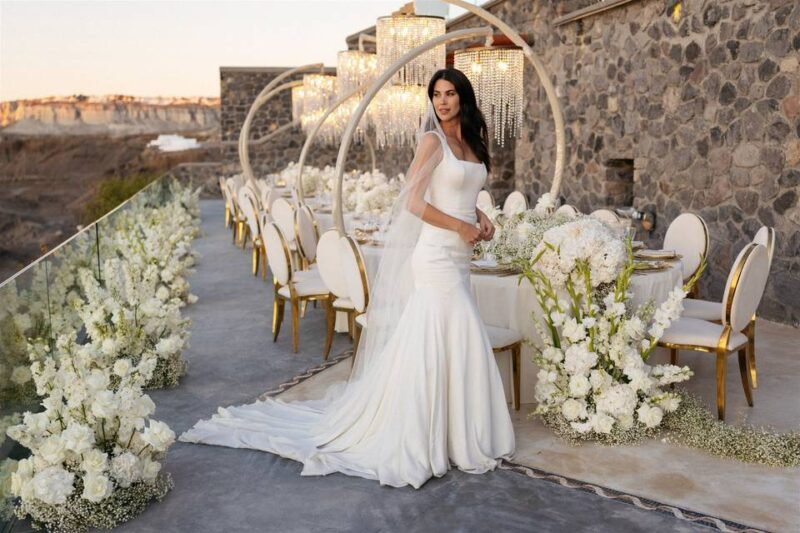 a bride posing in front of flowers and a wedding table at her santorini wedding