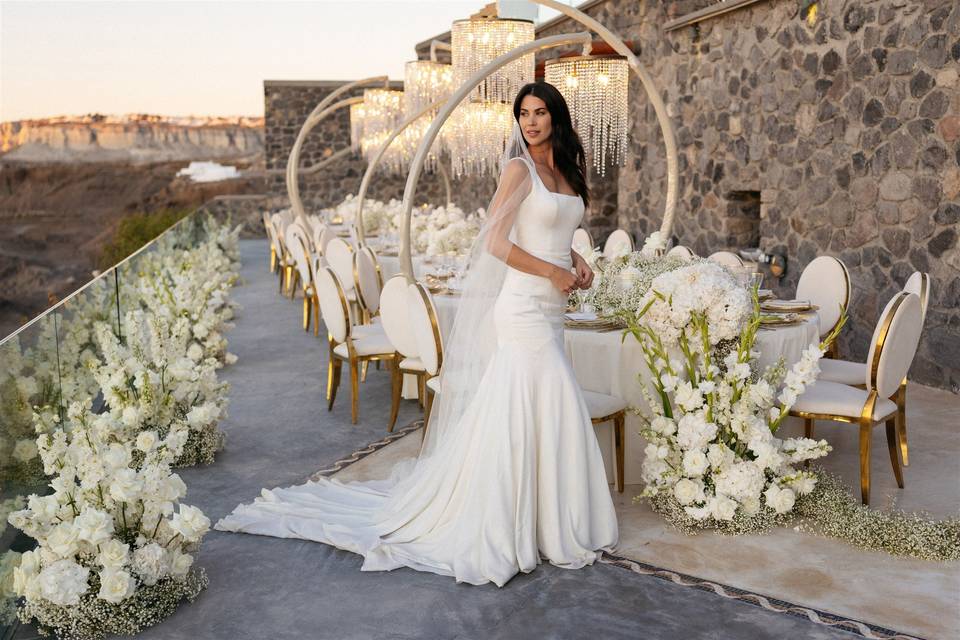 a bride posing in front of flowers and a wedding table at her santorini wedding