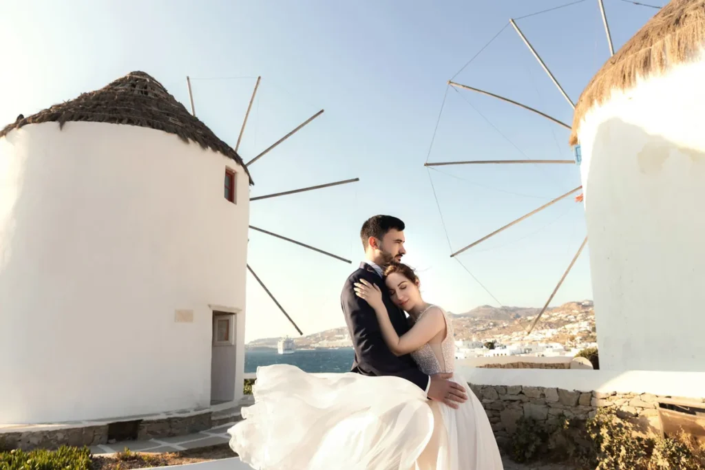 a newled couple embracing in front of the famous mykonos windmills