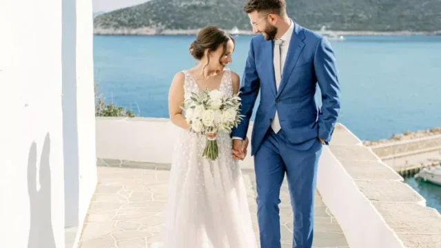 a newlywed couple in greece holding hands with the sea in the background