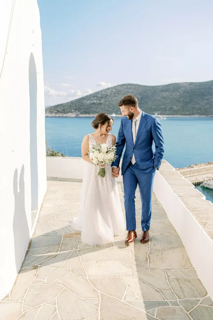 a newlywed couple in greece holding hands with the sea in the background