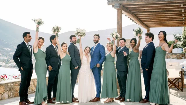 a wedding party in greece with bridesmaids in green tones, a bride in white, and the groom in blue