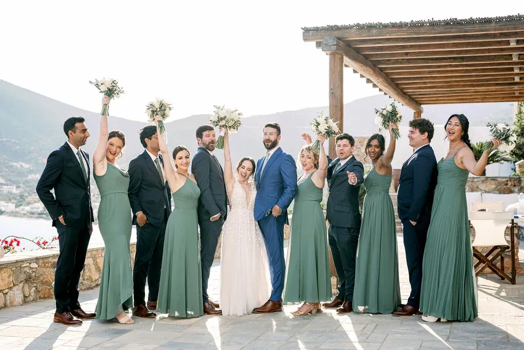 a wedding party in greece with bridesmaids in green tones, a bride in white, and the groom in blue