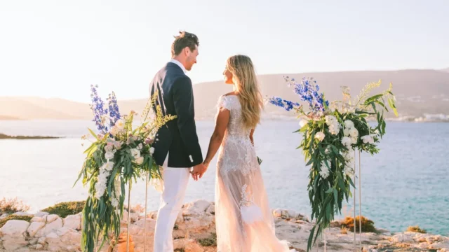 A newlywed couple holding hands with the sea behind them
