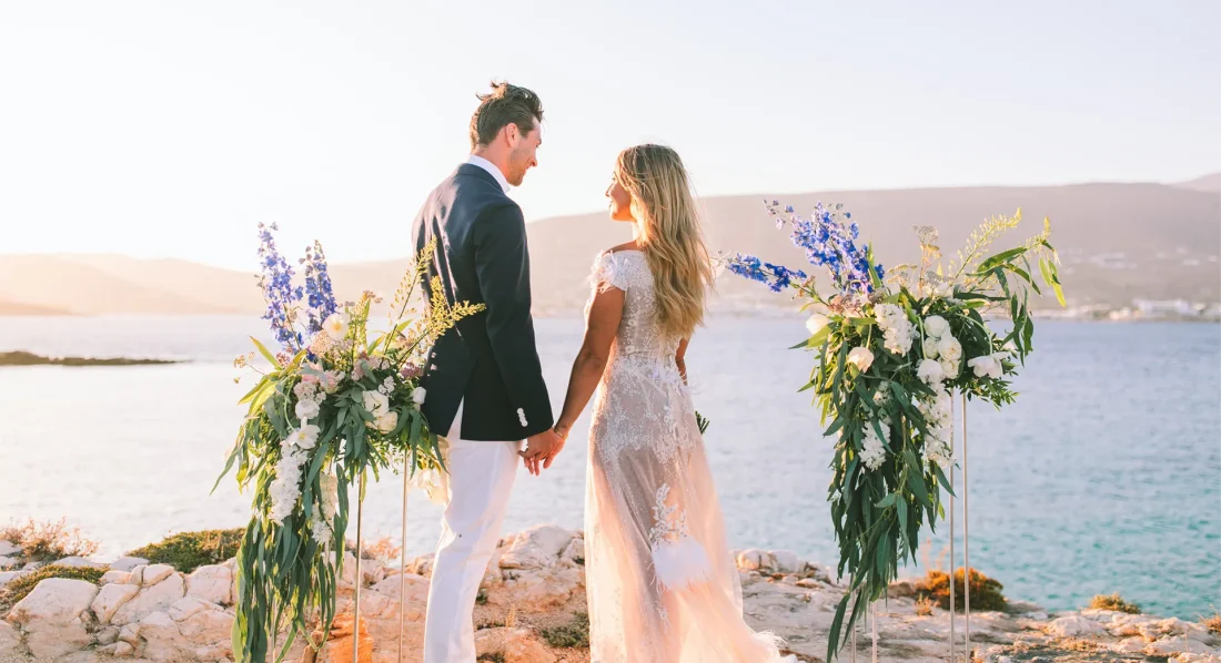 A newlywed couple holding hands with the sea behind them