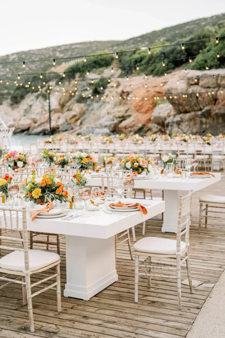 a number of wedding tables set in front of the greek sea and hills