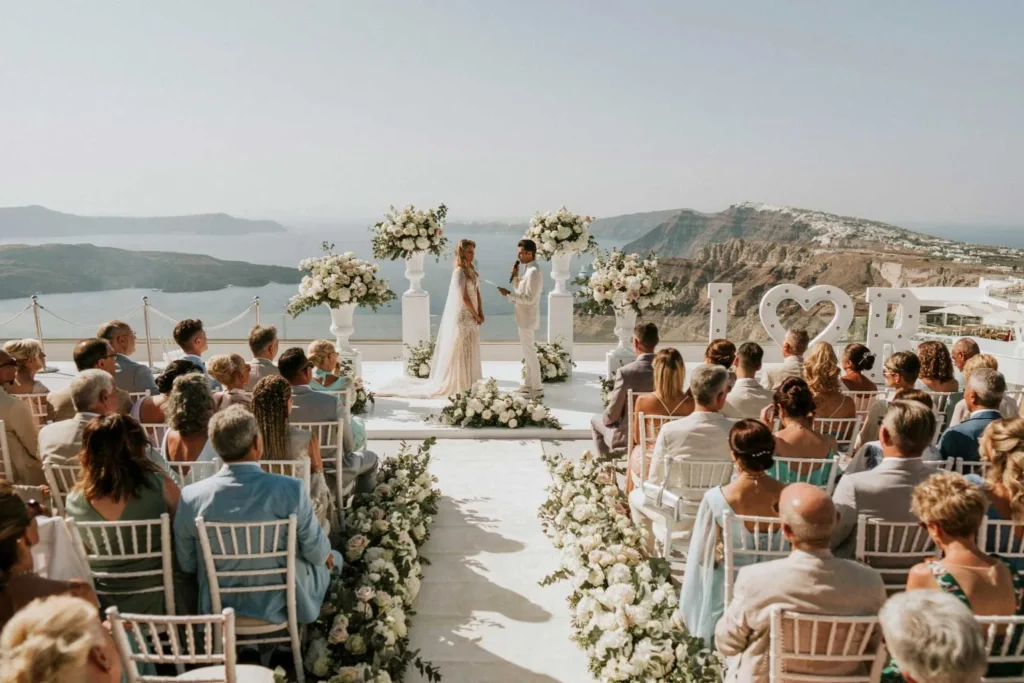 a packed outdoor wedding ceremony in santorini with the bride and groom at the altar in front of the caldera view