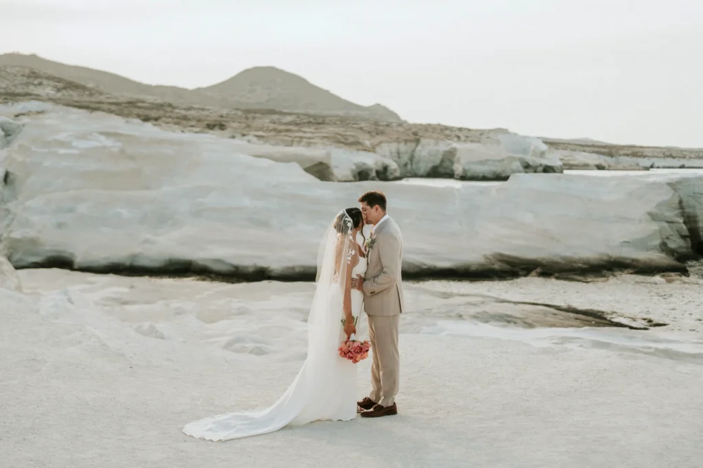 a wedding couple  at an intimate wedding kissing near the beach on milos