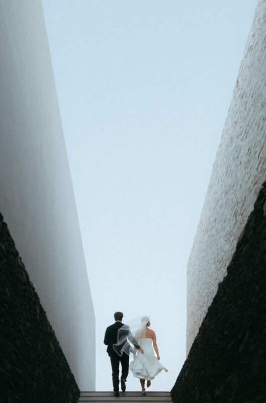 Couple walking up steps between two tall walls towards the open sky