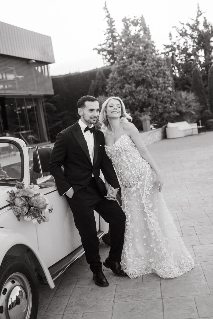 Black and white photo of a couple leaning against a vintage car decorated with flowers