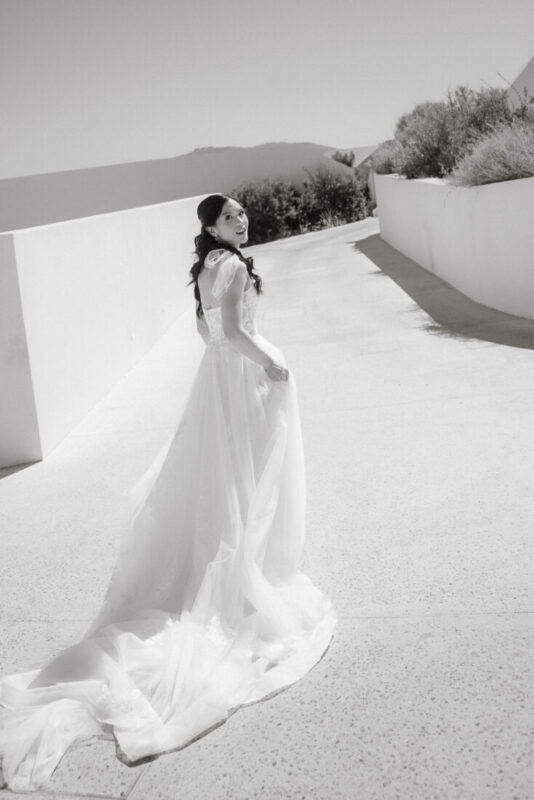 Black and white photo of a bride looking back over her shoulder, her long train spread on the ground