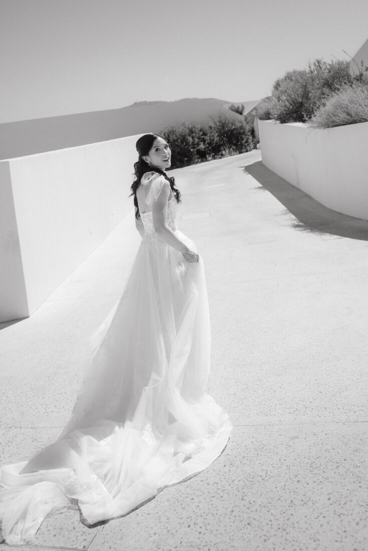 Black and white photo of a bride looking back over her shoulder, her long train spread on the ground