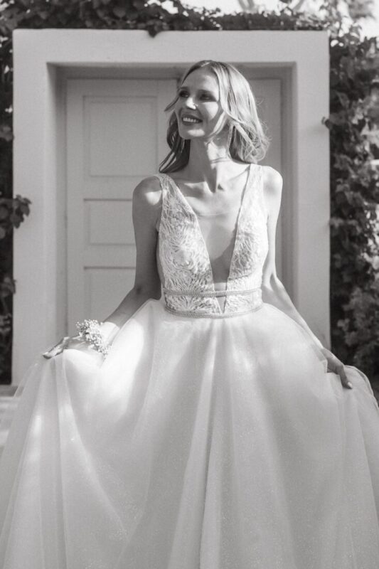 Black and white photo of a smiling bride in a lace gown in front of a white door