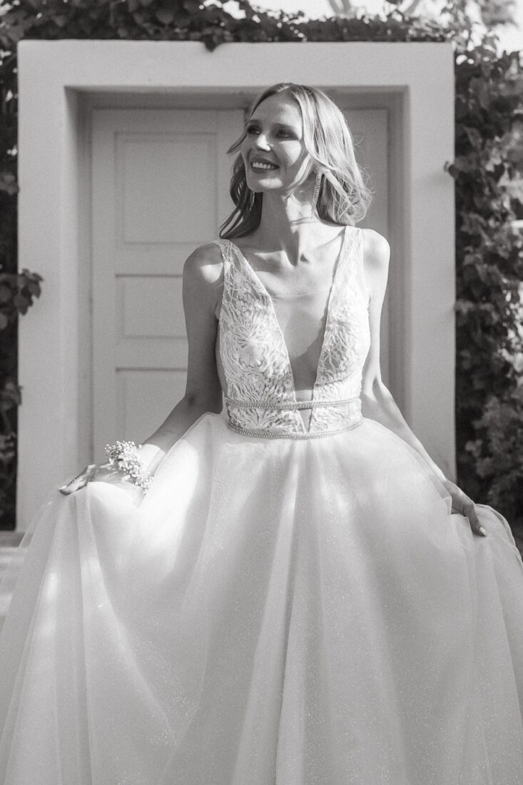 Black and white photo of a smiling bride in a lace gown in front of a white door