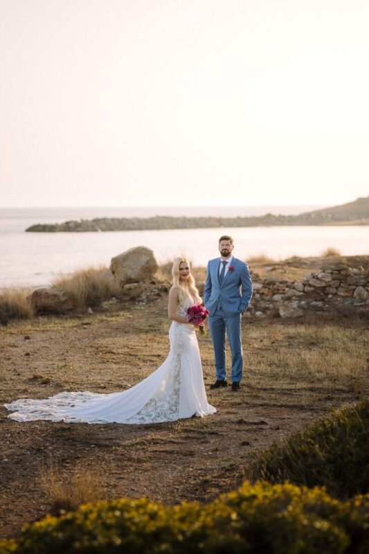Couple on a grassy headland by the sea at sunset, the bride's long train spread on the ground