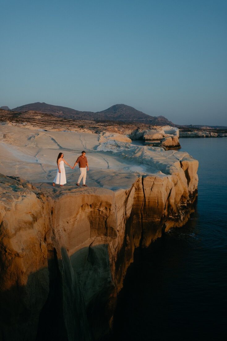 Couple holding hands on pale rock cliffs above the sea at dusk